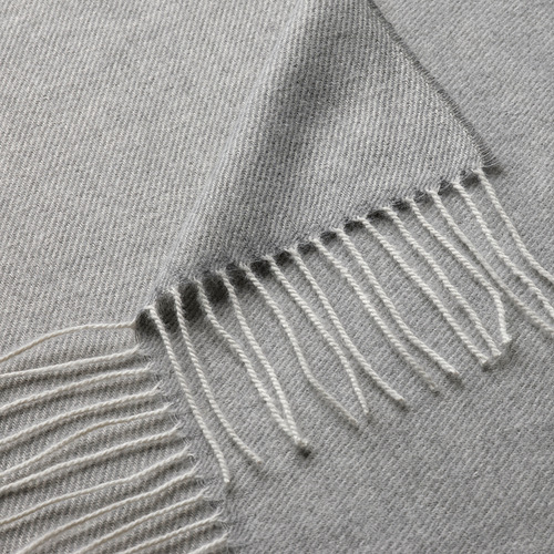 Manta suave y gris con flecos intrincados y espaciados uniformemente a lo largo del borde.