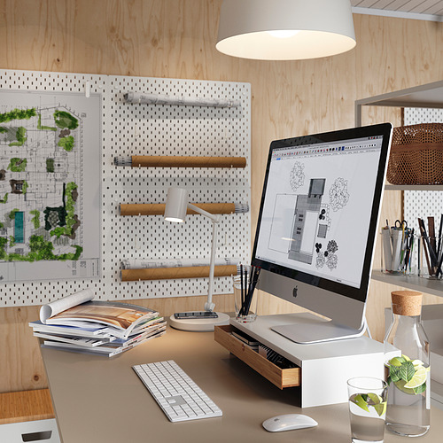 Escritorio de oficina en casa con imac, teclado, ratón, lámpara y libros. Tablero perforado con planos y arte. Decoración blanca y de madera.