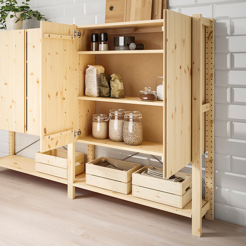 Estantería de madera con puertas abiertas, con tarros de granos y bolsas de papel, con un suelo de madera clara y un fondo de pared de ladrillo.