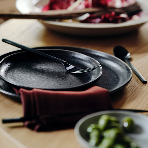 Plato de gres negro mate con palillos, más pequeños que los cuencos cercanos, sobre una mesa de madera.