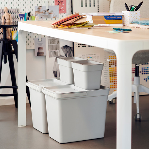 Un espacio de trabajo moderno con un sistema de clasificación de contenedores de residuos HÅLLBAR blanco. Los contenedores son apilables, están hechos de plástico reciclado y están diseñados para la organización.