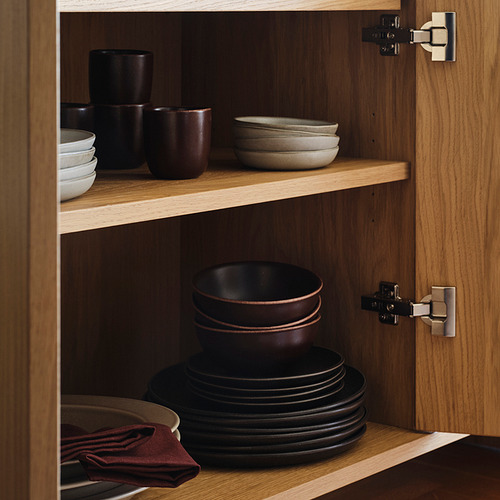 Armario de madera con puertas abiertas, que muestra dos estantes llenos de platos y tazas de color marrón oscuro, cuidadosamente organizados.