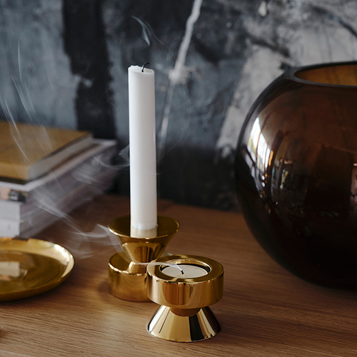 Candelabros dorados sobre una mesa de madera. Uno sostiene una vela blanca que emite humo.