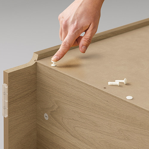 Una mano colocando tacos blancos sobre una estantería BILLY, de color marrón claro y hecha de tableros de partículas, con estantes ajustables y una textura de madera.