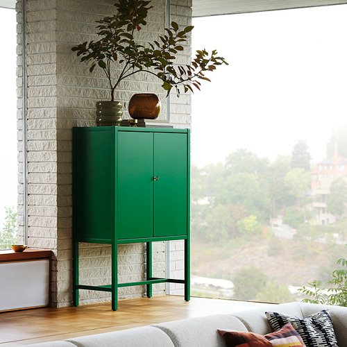 Armario STOCKHOLM 2025 de color verde brillante con llave de latón, grande y alto, colocado cerca de la ventana, el jarrón y la planta.