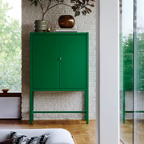 Armario verde STOCKHOLM 2025, moderno y alto, junto a grandes ventanales con estantes.