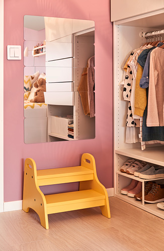 Un taburete amarillo para niños se encuentra en una habitación rosa junto a un armario con perchas y estantes.