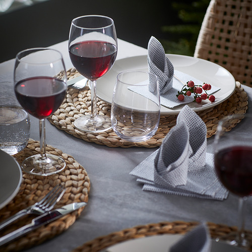Mesa con grandes copas de vino, platos, cubiertos y manteles individuales tejidos.