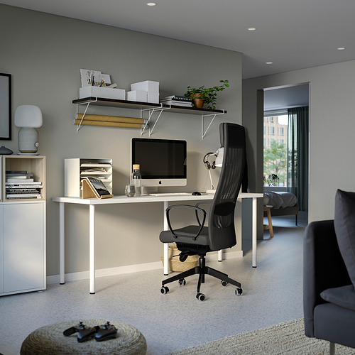 Configuración de oficina en casa con escritorio blanco, silla negra, computadora, estantes y lámpara.