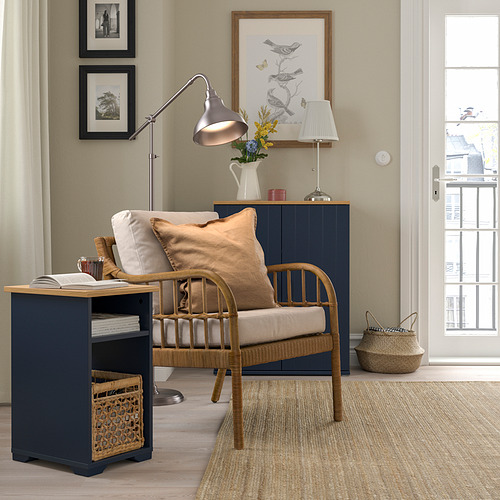 Acogedor rincón con mesa auxiliar azul marino SKRUVBY, silla de mimbre, lámpara y arte. Las mesas contrastan con el color oscuro con la decoración clara, encajando perfectamente junto a la silla.