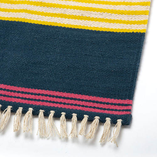 Alfombra tejida a mano con rayas vibrantes de amarillo, blanco y rojo sobre azul oscuro. Flecos en los bordes, que muestran la artesanía de calidad.
