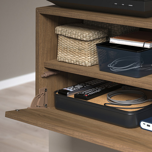 Mueble de TV de madera con compartimento frontal abatible para el mando a distancia y los cables. Los estantes superiores contienen cestas de mimbre y un contenedor negro.