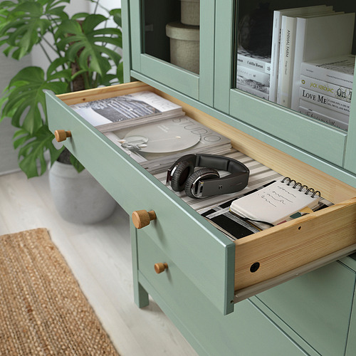 Cajón verde del armario abierto, revelando auriculares, libros y cuadernos.