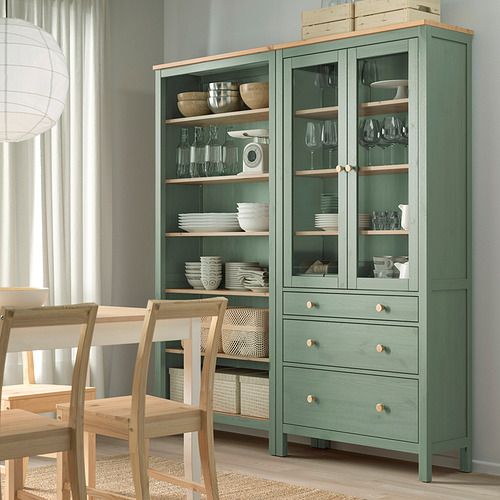 Almacén de madera verde HEMNES. La unidad alta exhibe cristalería, tazones, platos. Cajones de madera, puertas de cristal. Alto, combina con las sillas de comedor.