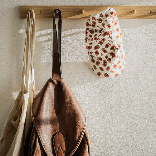 Tres bolsos en un perchero de madera: bolso marrón con asa negra, lona beige, manchas rojas y blancas.