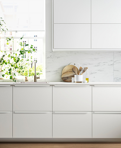Cocina blanca moderna con líneas limpias y salpicadero de mármol. Gabinetes elegantes y fregadero de acero inoxidable. La planta agrega verdor.