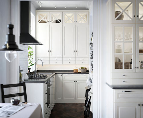 Cocina moderna blanca con gabinetes de color blanquecino, encimera gris, fregadero de acero inoxidable, campana negra y armarios de vidrio.