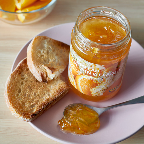 Un tarro de mermelada de naranja, dos rebanadas de pan y una cucharada de mermelada en un plato rosa.