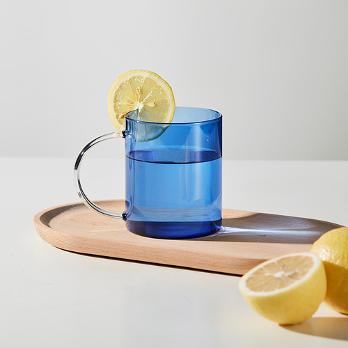 Taza azul con asa curva en la bandeja, rodaja de limón en el borde y medio limón al lado, sugiere una bebida con limón.