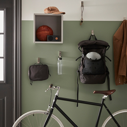 Una pared verde en un pasillo muestra una bicicleta, una mochila, un abrigo y una botella de agua con una correa.