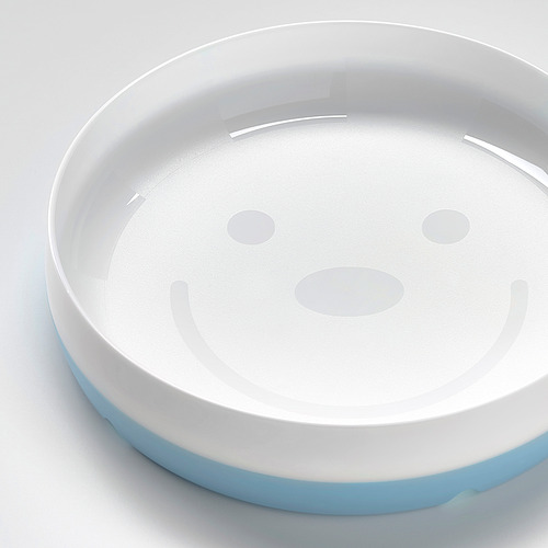 Plato redondo, blanco con borde azul, diseñado para niños. Cara sonriente, base antideslizante y lados en ángulo para comer fácilmente.