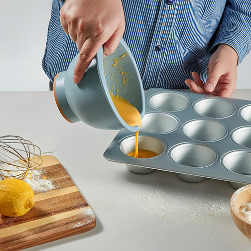 Persona vertiendo masa amarilla de un tazón para batir en un molde para muffins.