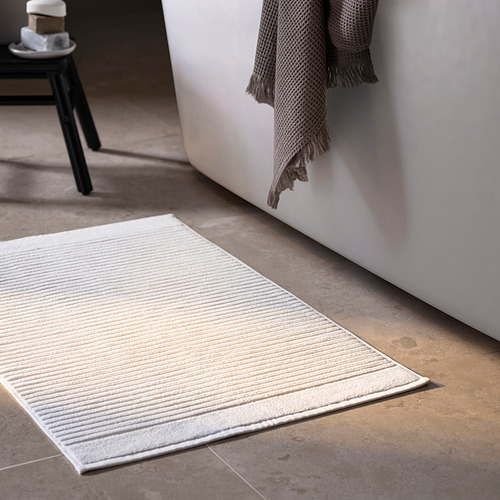 Baño con alfombra de rizo blanco, toalla gris, taburete negro.