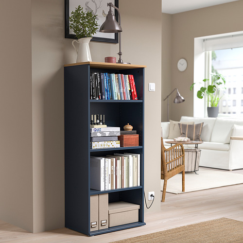 Librería negra SKRUVBY con tapa de madera, que sostiene libros y decoración. Alto, se adapta a la esquina de la acogedora sala de estar, cerca de paredes beige y muebles blancos.
