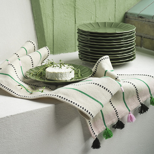 Plato glaseado verde con queso y hierbas, junto a una pila de platos sobre mantel a rayas.
