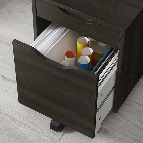 Escritorio de madera oscura con cajón abierto que muestra tubos y papeles de colores, con ruedas para facilitar el movimiento.