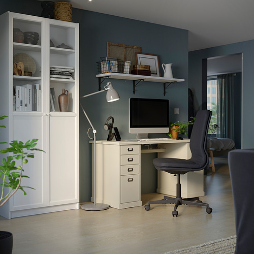 Neat home office with white BILLY bookcase and desk. Dark teal wall, grey chair, computer, lamp, and plant.