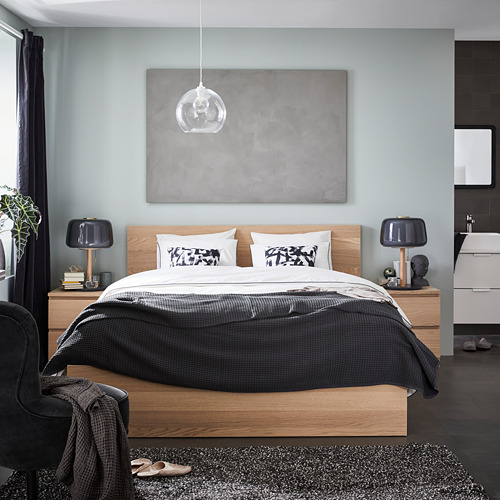 Dormitorio moderno con paredes grises, estructura de cama de madera, ropa de cama blanca y negra, dos mesitas de noche con lámparas y un gran cuadro abstracto sobre la cama.