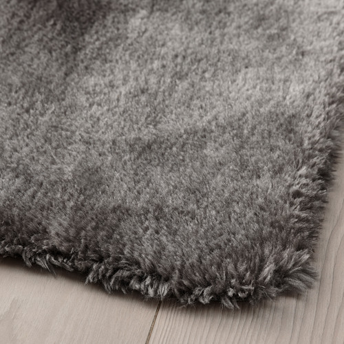 Primer plano de una alfombra gris suave y afelpada con superficie texturizada y peluda sobre suelo de madera.