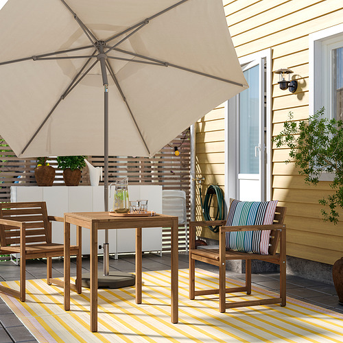 Acogedor patio con sombrilla, mesa, sillas y alfombra junto a una casa amarilla.