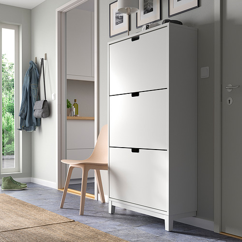 Zapatero STÄLL blanco moderno cerca de la puerta gris, con ganchos para colgar y una silla.