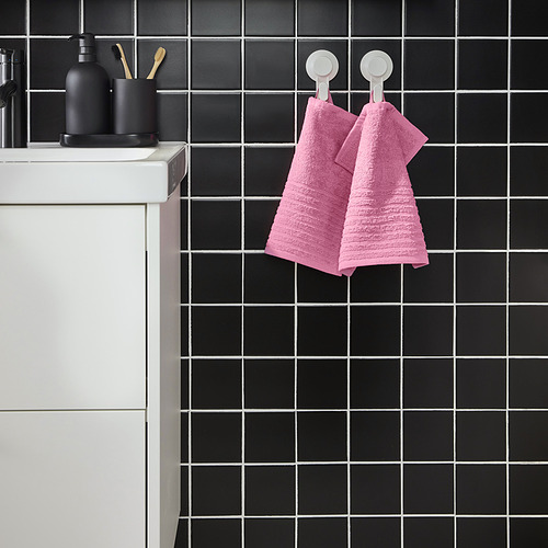 Baño moderno con azulejos negros, toallas VÅGSJÖN rosas, lavabo blanco, accesorios negros.