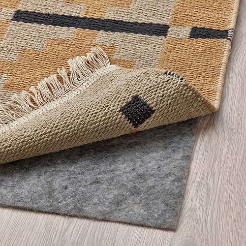 Alfombra geométrica beige y negra con flecos, doblada para mostrar la parte inferior, ideal para comedores y salones.