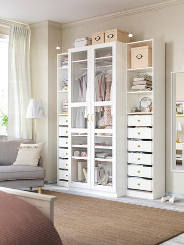 Un dormitorio bien organizado con un armario blanco TYSSEDAL con puertas de cristal que revelan ropa y objetos cuidadosamente dispuestos.