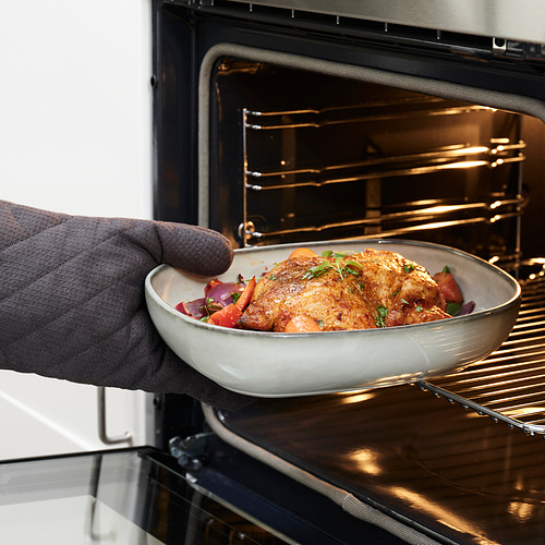 La persona coloca el pollo asado y las verduras en la fuente del horno.