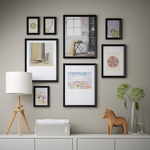Una pared con fotos, arte y decoraciones enmarcadas sobre un armario blanco.