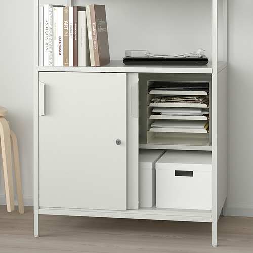 Un armario TROTTEN blanco con estantes ajustables almacena libros, archivos y una caja, con puertas correderas en un lado para un almacenamiento cerrado.
