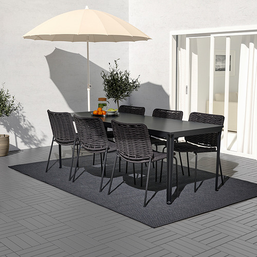 Juego de mesa y sillas de exterior negras, con sombrilla beige en patio embaldosado, ideal para pequeñas reuniones.