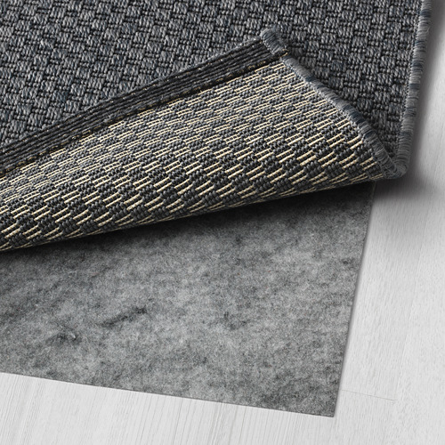 Alfombra tejida gris con respaldo visible, colocada sobre un piso de madera, mostrando su textura y diseño.