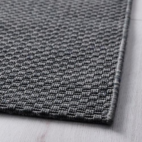 Vista en primer plano de una alfombra gris oscuro de tejido plano con textura visible sobre un suelo de madera.