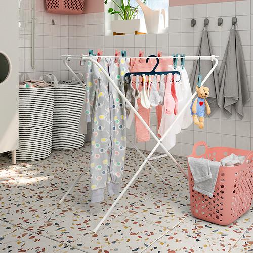 Tendedero blanco con ropa multicolor, cestas de lavandería grises y rosas, peluche colgante, paredes y piso de azulejos pintados de rosa.