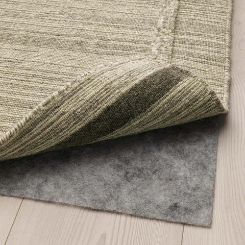 Una esquina de una alfombra con una gruesa capa inferior de fieltro gris visible, que muestra una característica antideslizante para mayor estabilidad y protección.