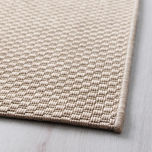 Alfombra tejida suave de color beige sobre suelo de madera, que muestra una textura y un diseño de calidad.