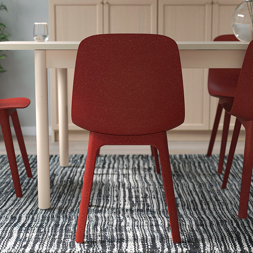 La silla roja con respaldo y patas lisas se coloca cerca de una mesa blanca, ideal para uso en interiores y asientos cómodos.