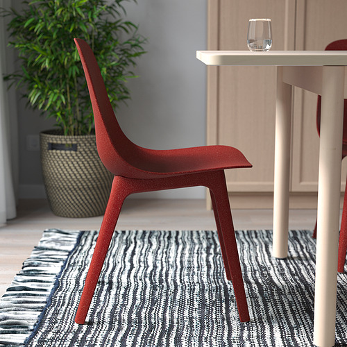 Silla roja con asiento y patas curvas. Colocado cerca de la mesa con vidrio y planta. Ideal para uso en interiores, se almacena fácilmente.