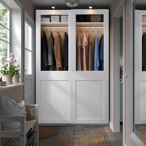 Open white wardrobe, PAX, showcasing clothes, stands tall next to window and bench. Modern and spacious.
